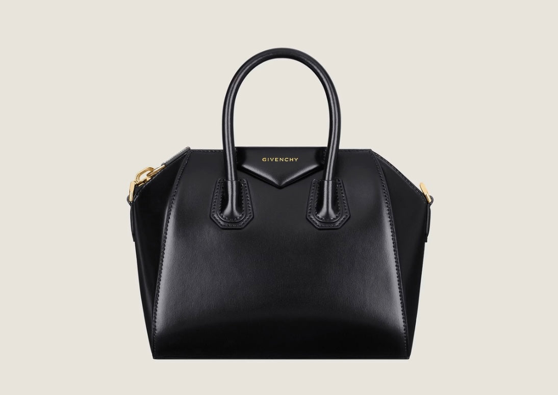 Black Givenchy Antigona handbag with structured angular sides, rounded top handles and gold-tone hardware against a pale background.