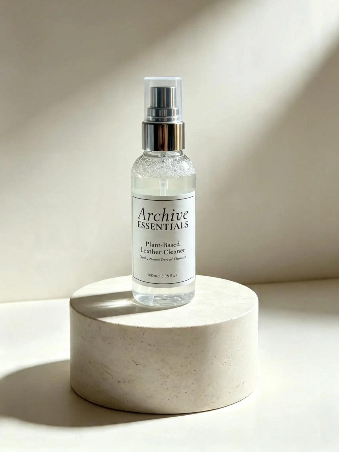 Archive Essentials Plant-Based Leather Cleaner bottle on a pale round display plinth.