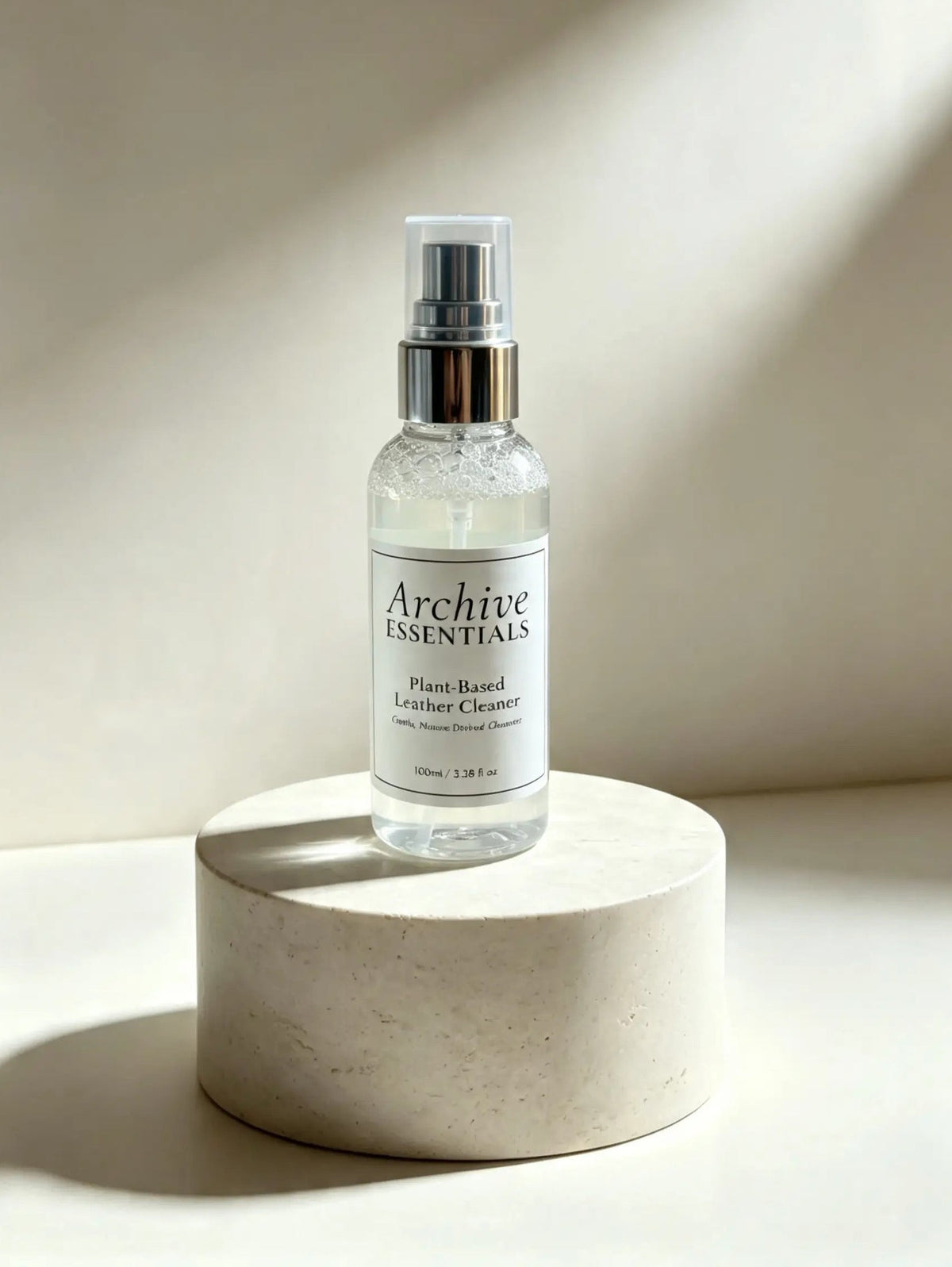 Archive Essentials Plant-Based Leather Cleaner bottle on a pale round display plinth.