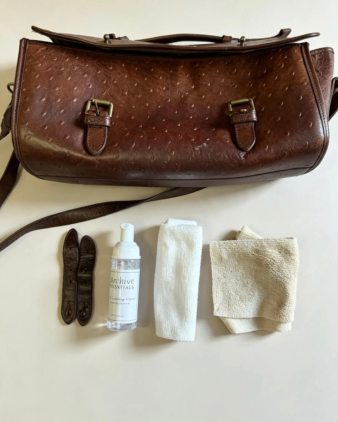 Brown leather handbag laid out with Archive Essentials cleaner and microfibre cloths before cleaning