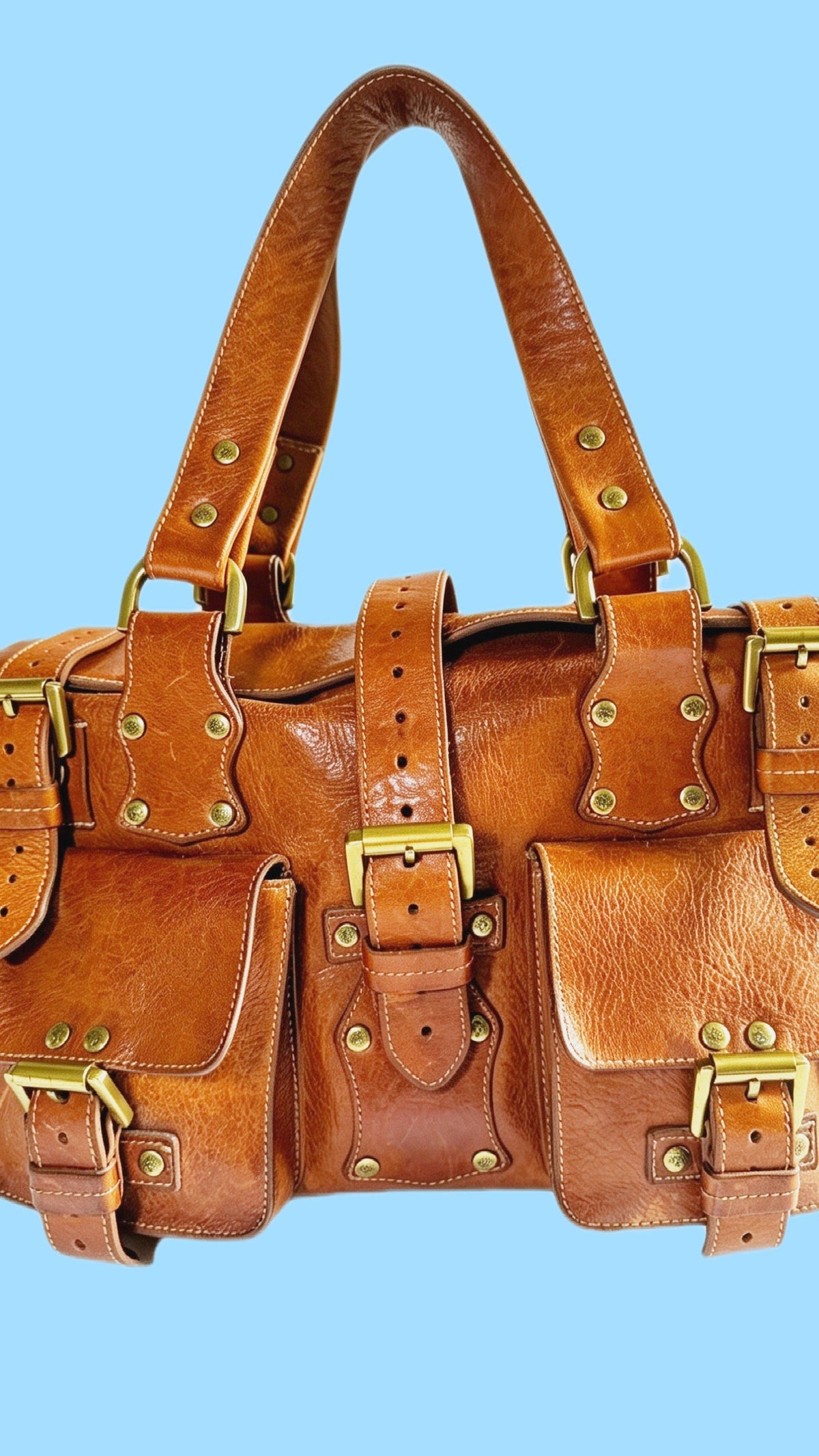 Tan Mulberry Roxanne handbag with buckled front pockets, studded straps and gold-tone hardware against a blue background.